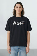 Person wearing a black t-shirt with 'Velvet' logo on a light background